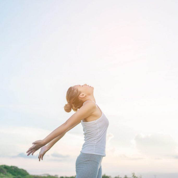 Young beautiful woman raising hands with beautiful view at meadow enjoy fresh air.